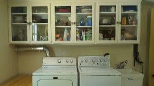 A laundry room featuring a washer and dryer beneath glass-front cabinets filled with various household items.