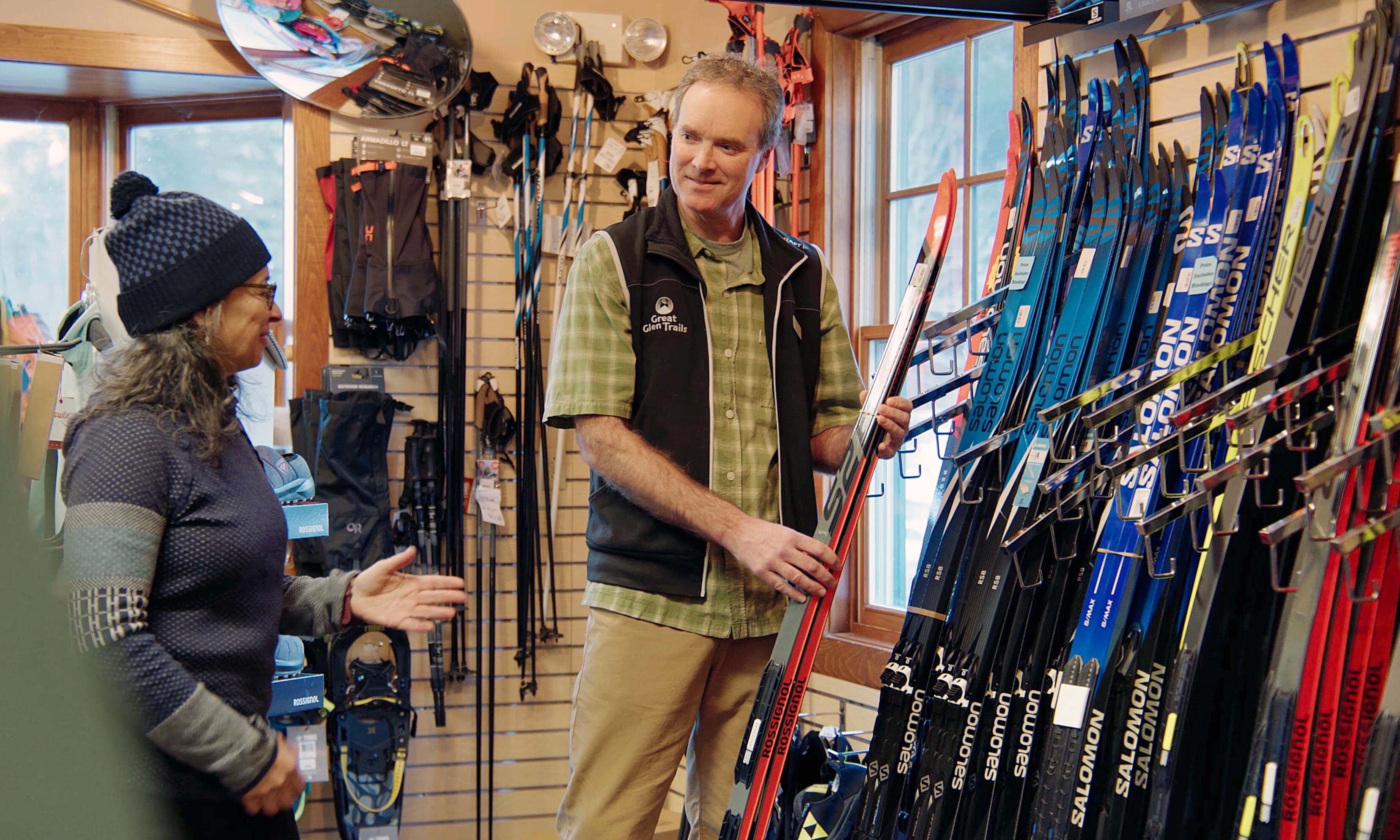 A man and a woman discuss skiing equipment in a well-stocked sports store.