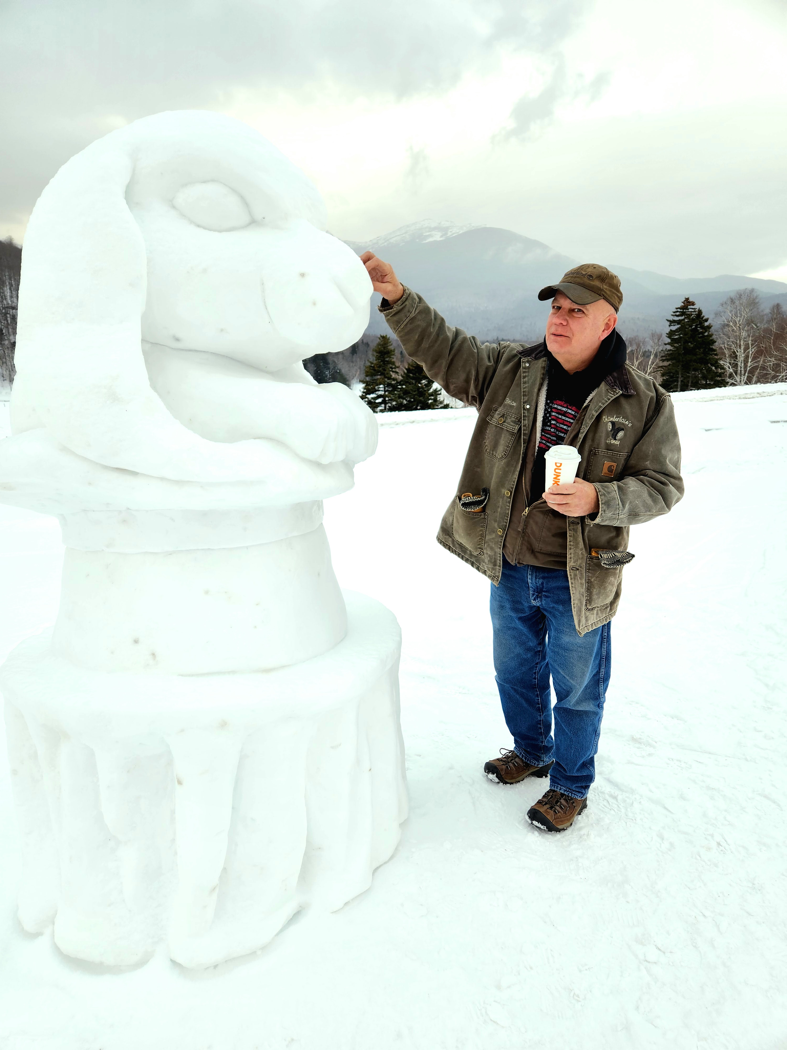 A man interacts with a large snow sculpture of a rabbit in a snowy landscape.
