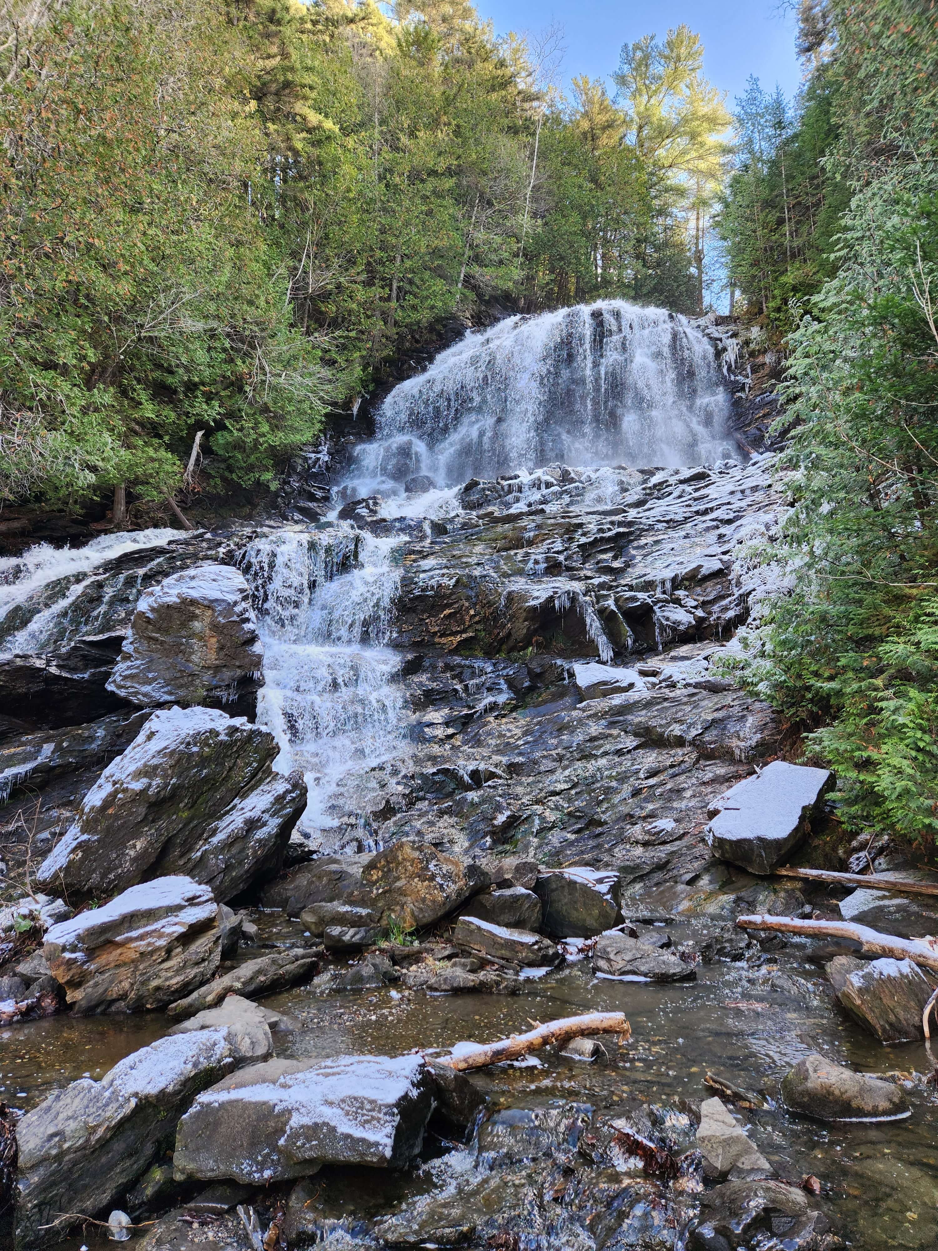 A cascading waterfall flows over rocky terrain surrounded by lush greenery.