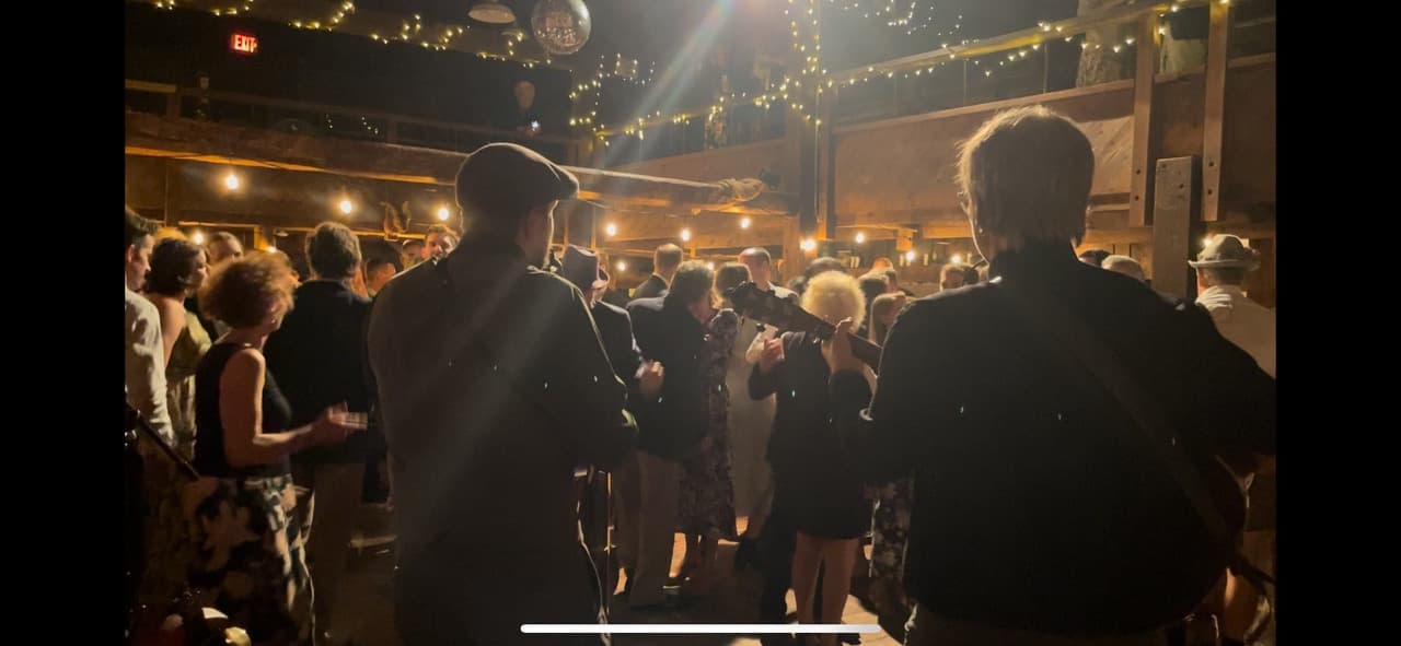 A lively crowd dances in a dimly lit venue with string lights and a festive atmosphere.