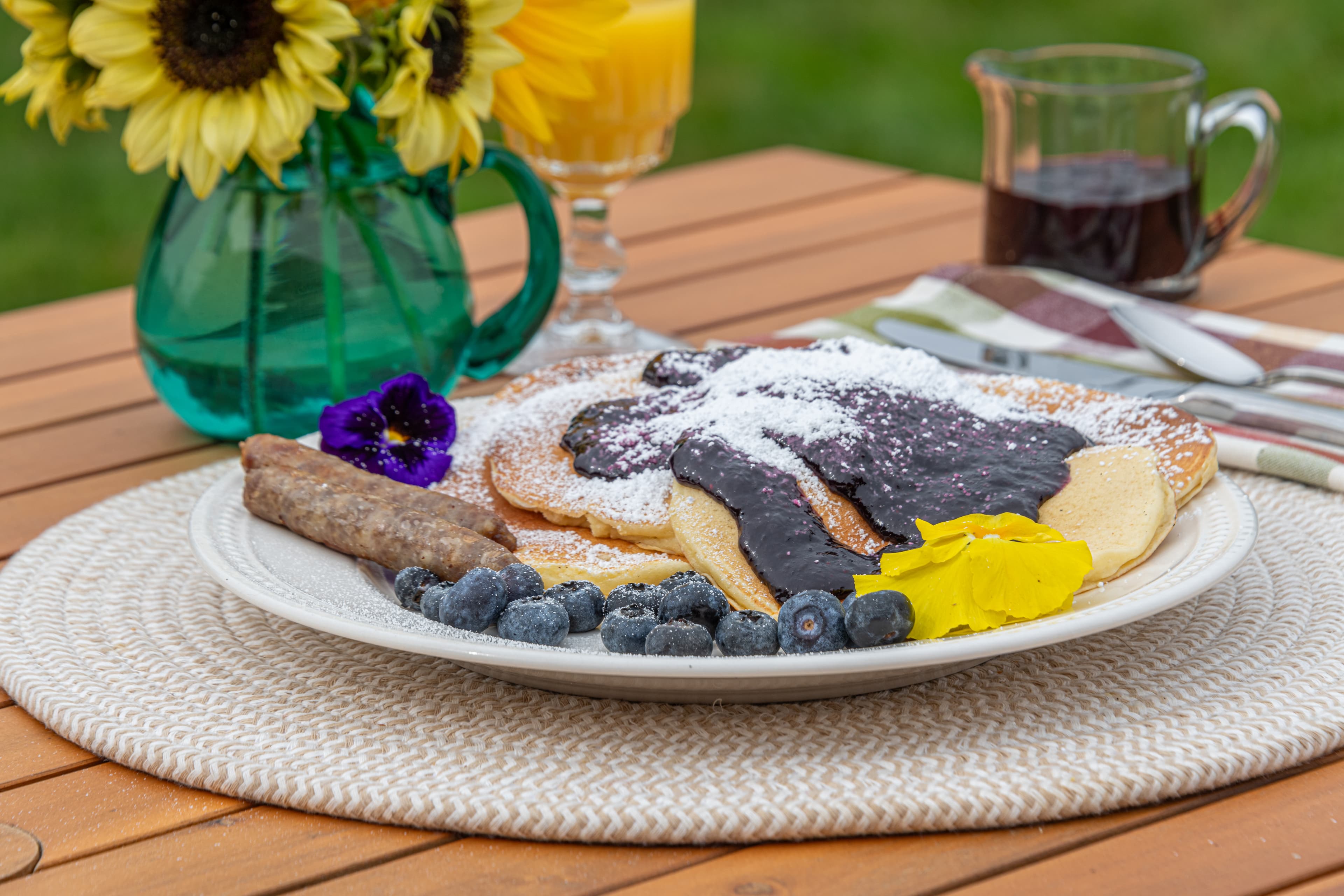 Lemon ricotta pancakes with blueberries, sausage links, on a table with a vase of yellow sunflowers.
