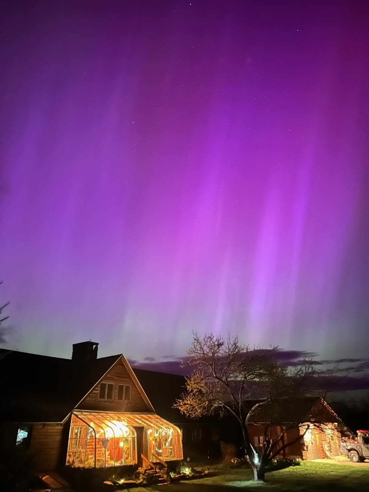 A glowing purple aurora stretches above a well-lit house at night.