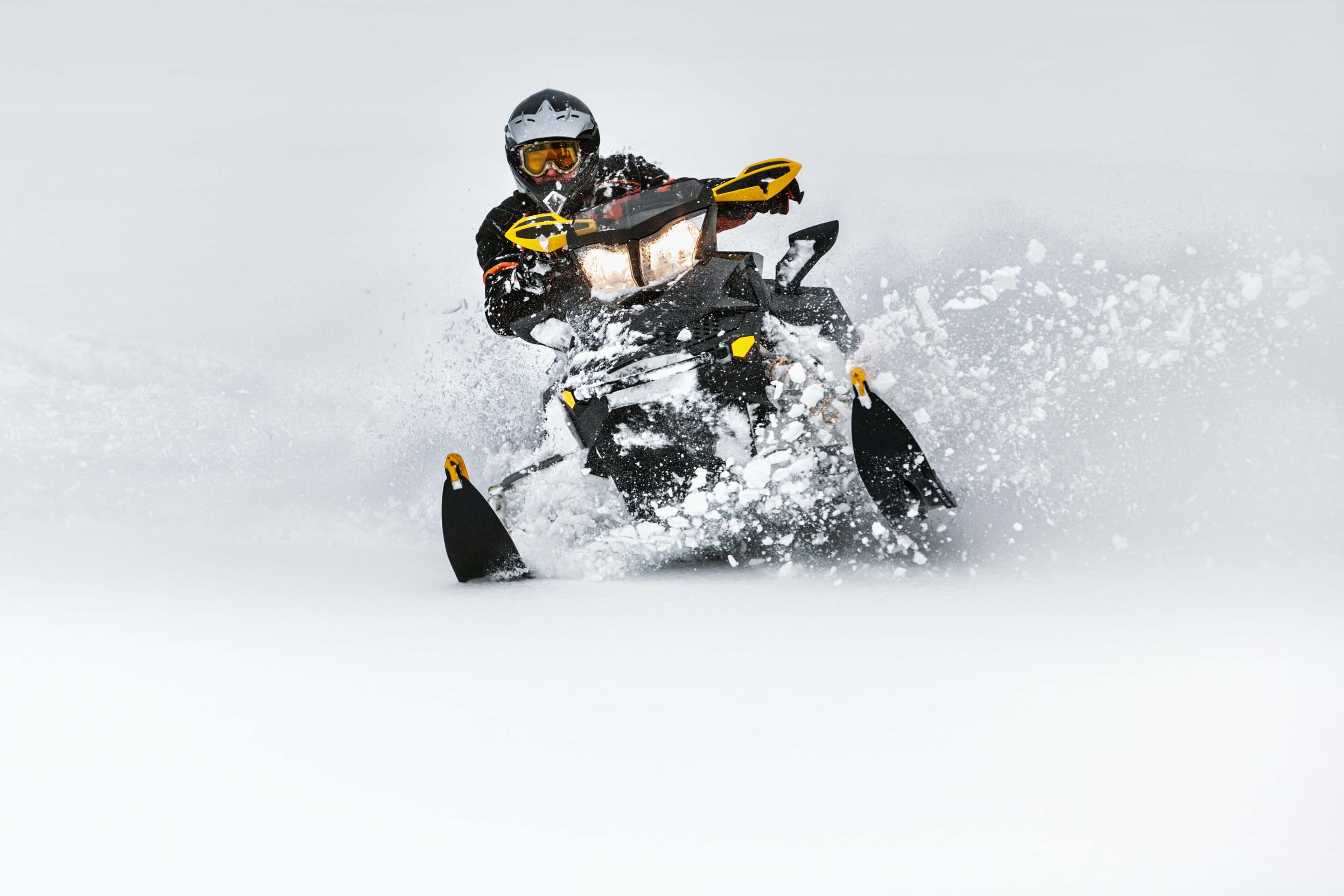 A person rides a snowmobile through deep snow, kicking up powder.