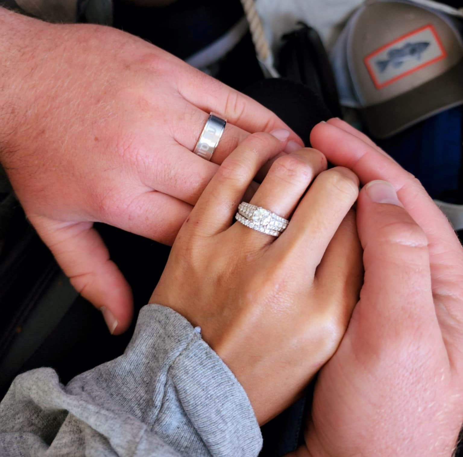Two hands hold each other, showcasing a diamond engagement ring and a wedding band.