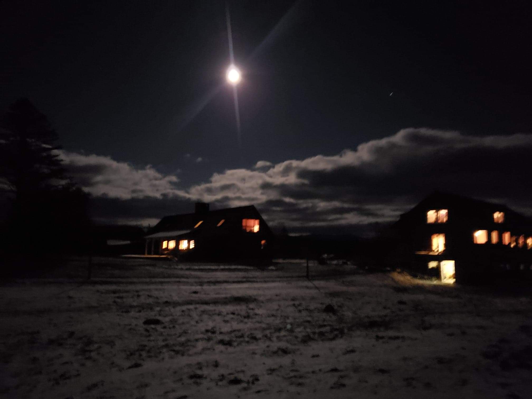 A moonlit night scene with two houses illuminated against a dark sky and snow-covered ground.