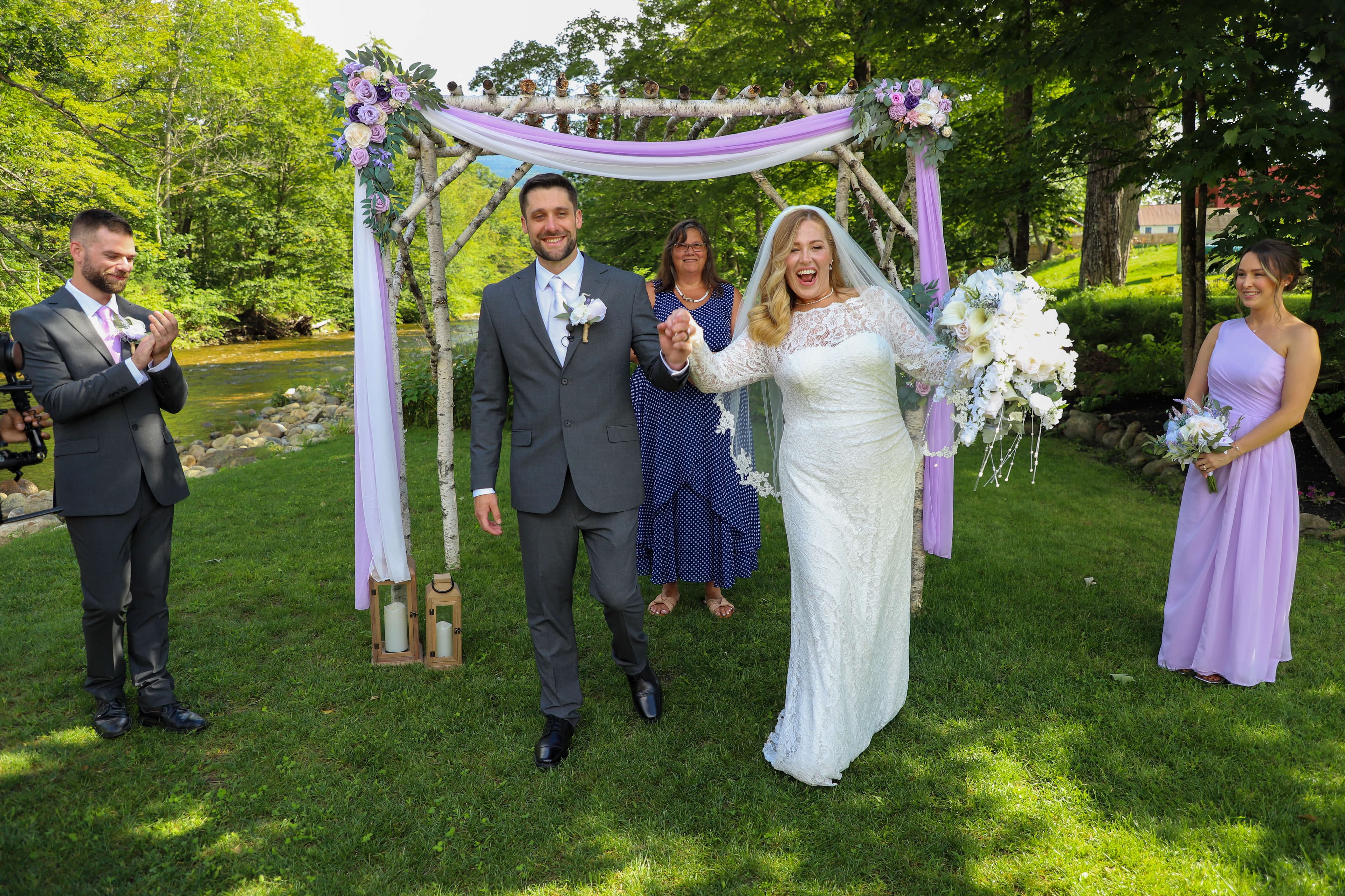 A happy couple walks hand-in-hand after their wedding ceremony, surrounded by friends in a scenic outdoor setting.