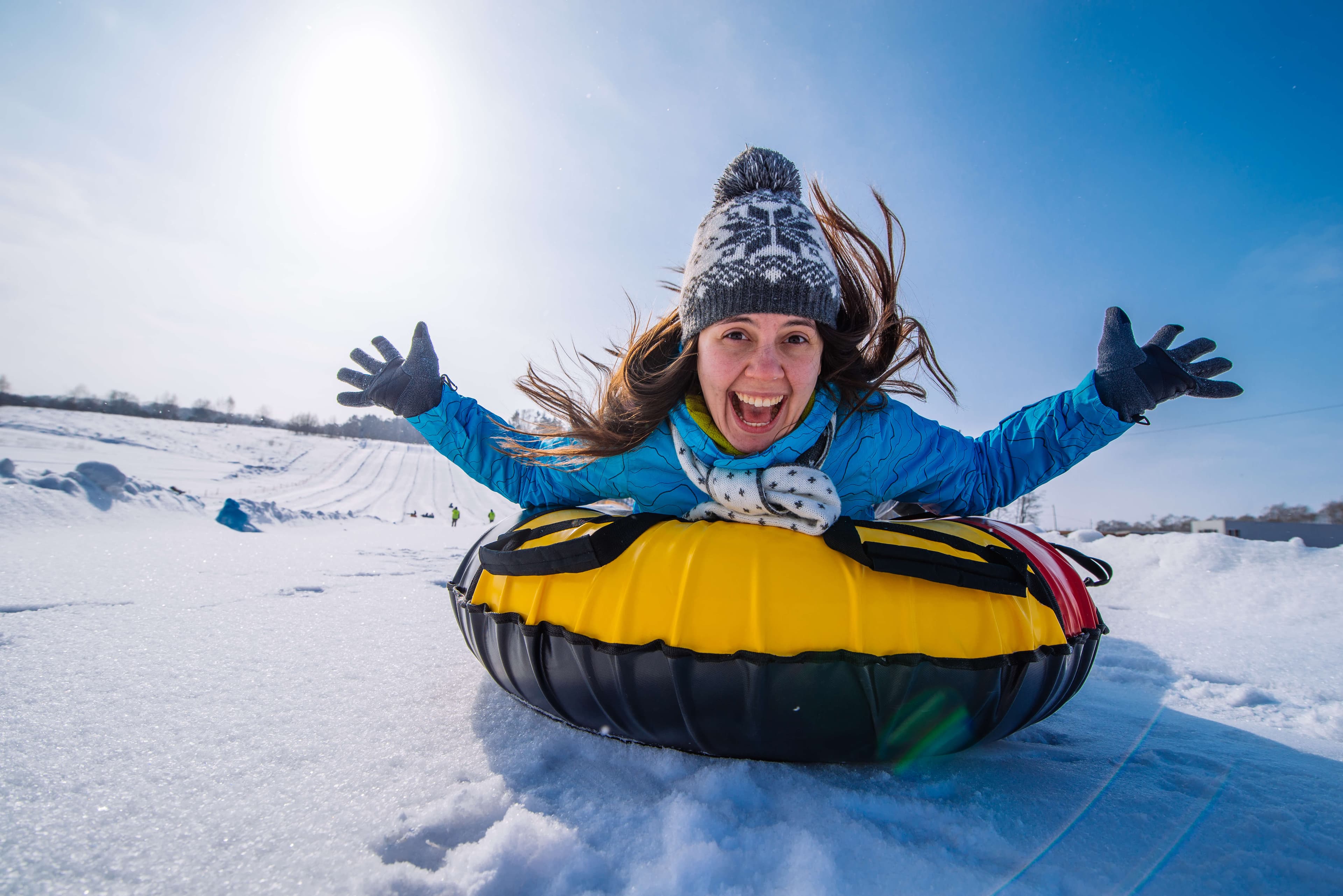 A woman joyfully sleds down a snowy hill on a yellow and black inner tube.