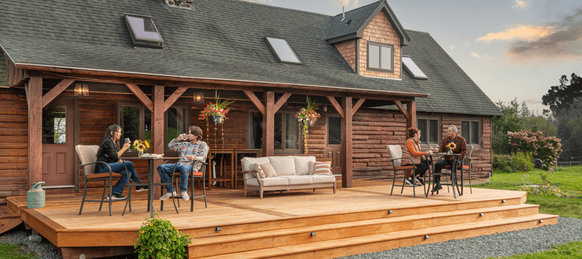 A wooden deck with people enjoying drinks and snacks outside a rustic house at sunset.