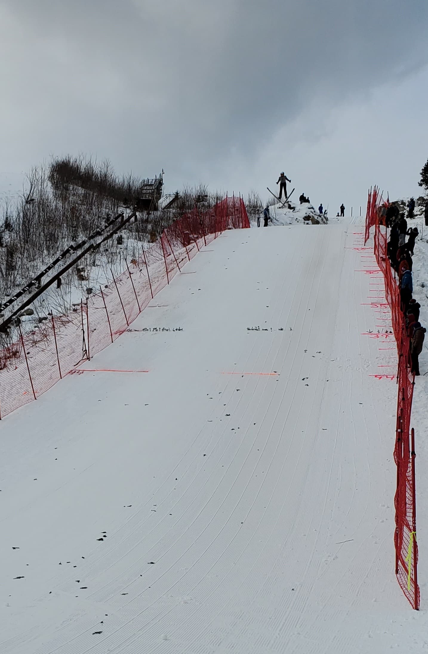 A ski slope lined with red safety fencing and spectators watching from the side.