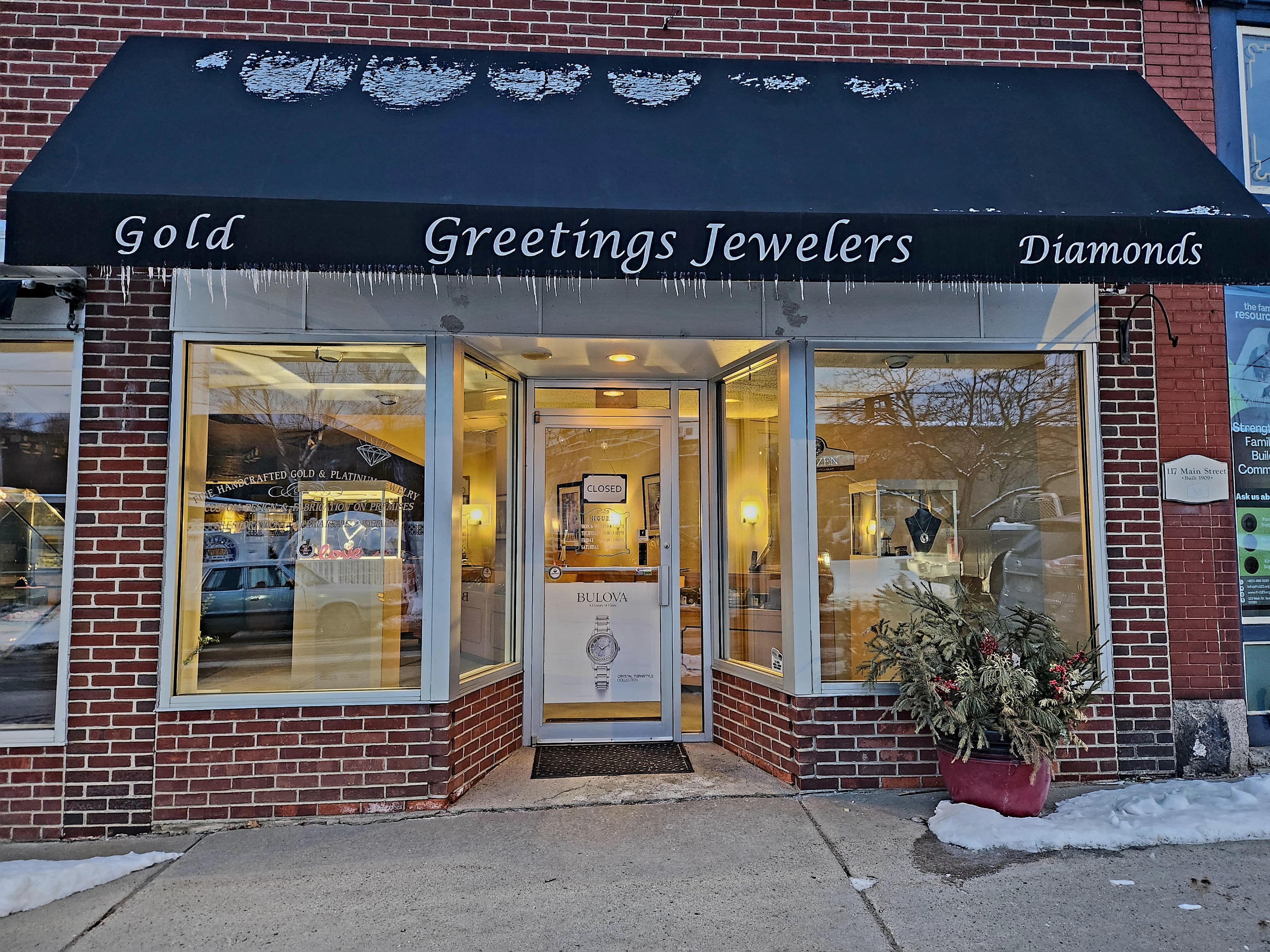 Storefront of Greetings Jewelers displaying jewelry inside and a sign in the doorway.