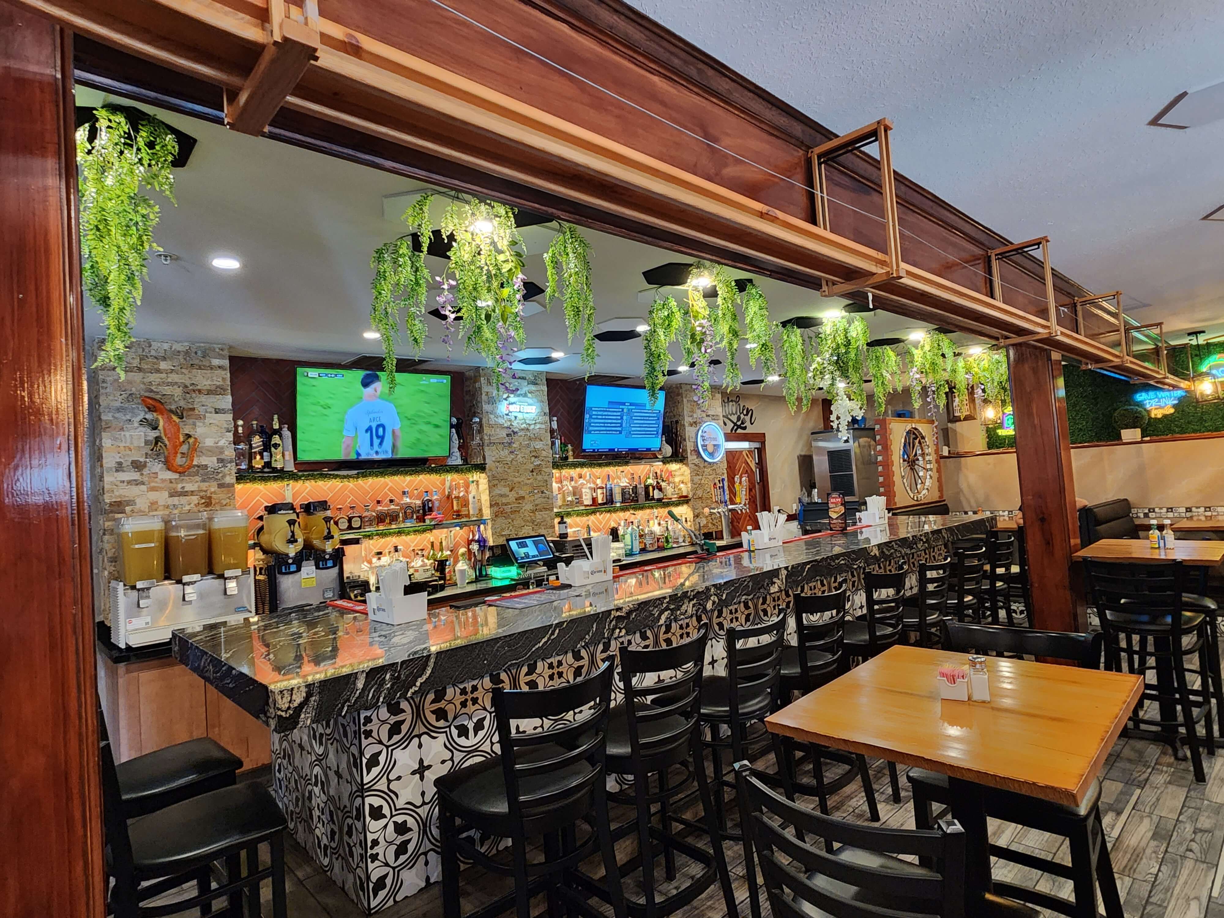 Interior of a vibrant bar with a polished counter, hanging plants, and a selection of drinks visible. Interior of a vibrant bar with a polished counter, hanging plants, and a selection of drinks visible.