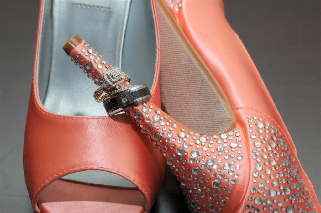 A close-up of coral high heels with sparkling embellishments and two rings resting on one of the shoes.