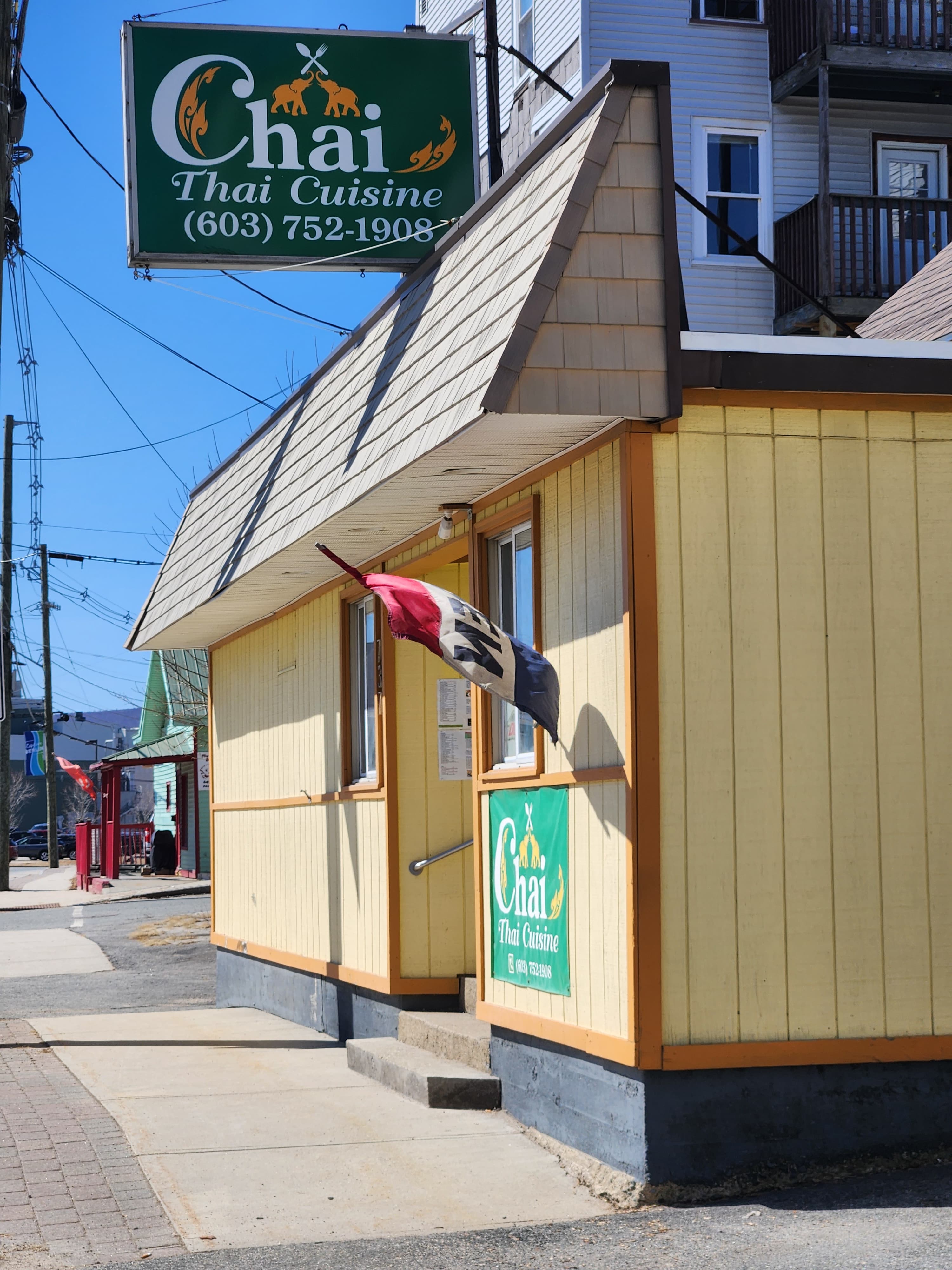 A small yellow building with a sign for "Chai Thai Cuisine" and a flag outside.