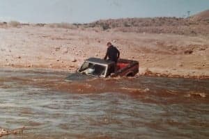 A person is standing on the roof of a partially submerged truck in a flood.