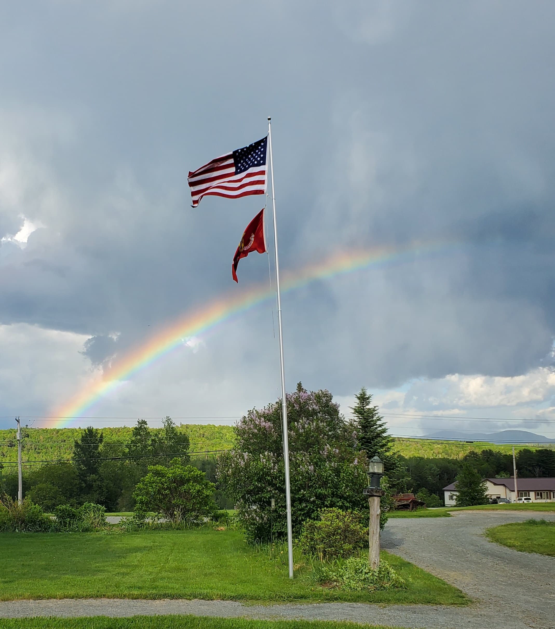A rainbow arcs over a landscape featuring American and other flags against a cloudy sky.