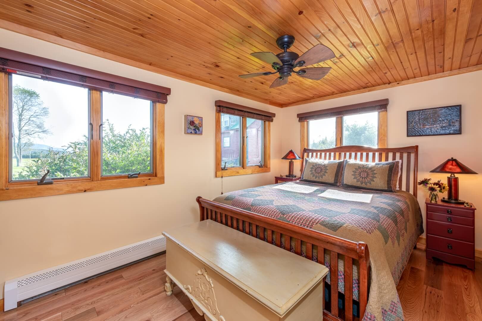 A cozy bedroom with a wooden ceiling, large windows, a quilted bedspread, and decorative accents.
