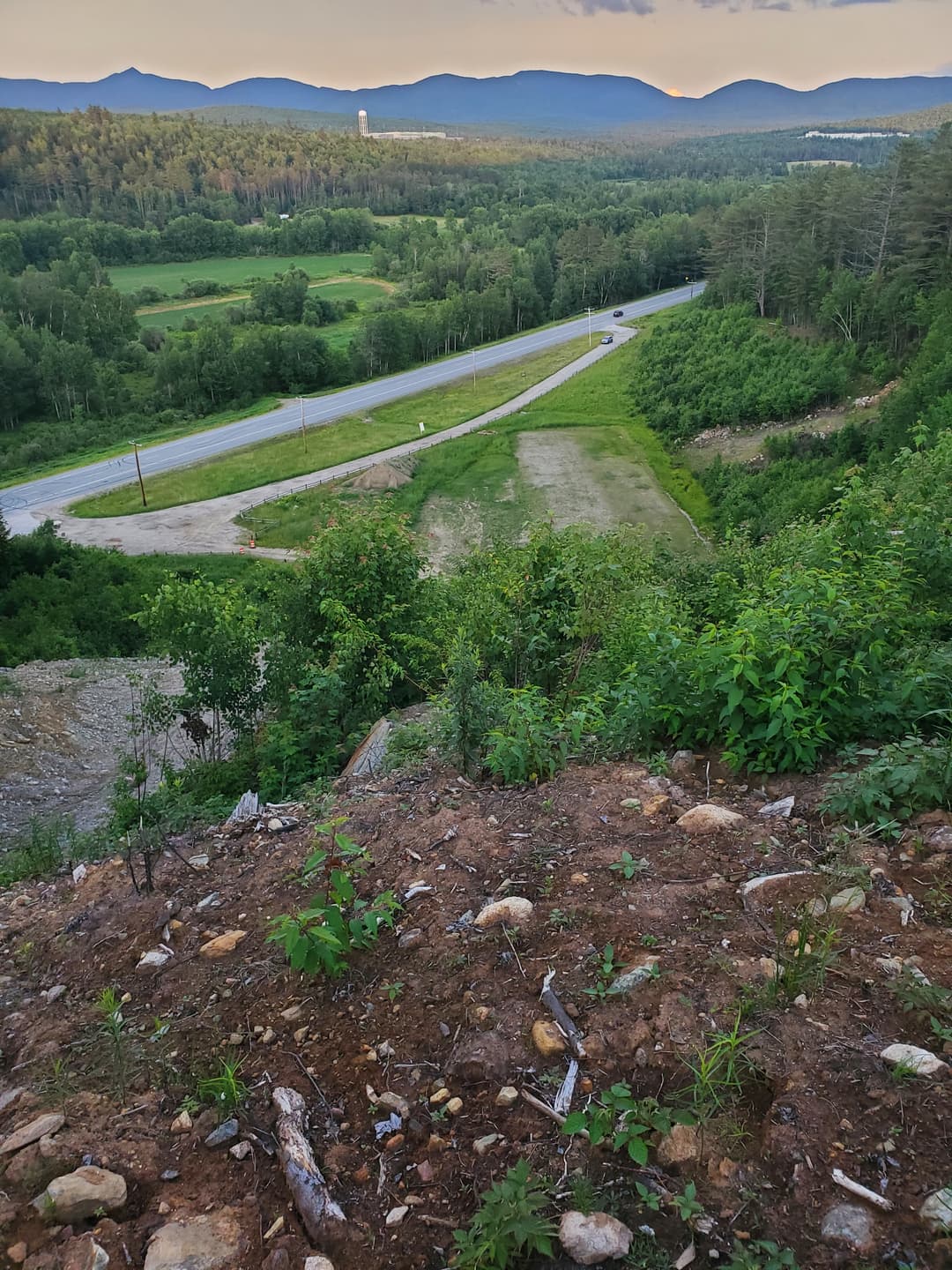 Elevated view from a hill overlooking a road, fields, and trees