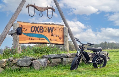 Ebike in front of Inn at Oxbow Acres sign. Sign is located beneath wood construct creating a triangle with ox yoke hanging from the apex.