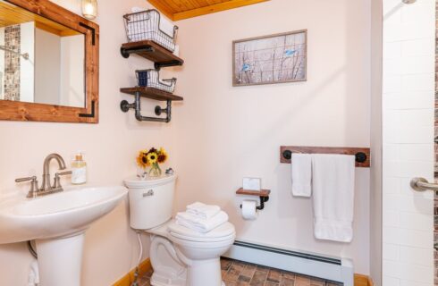 Large bathroom with pedestal sink, toilet and wooden shelves and mirrow