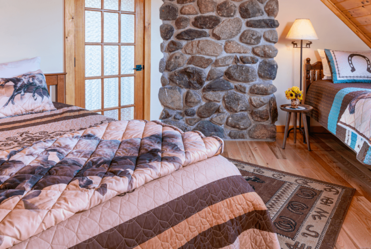 Queen and twin bed in front of a fieldstone chimney with horse throw blankets