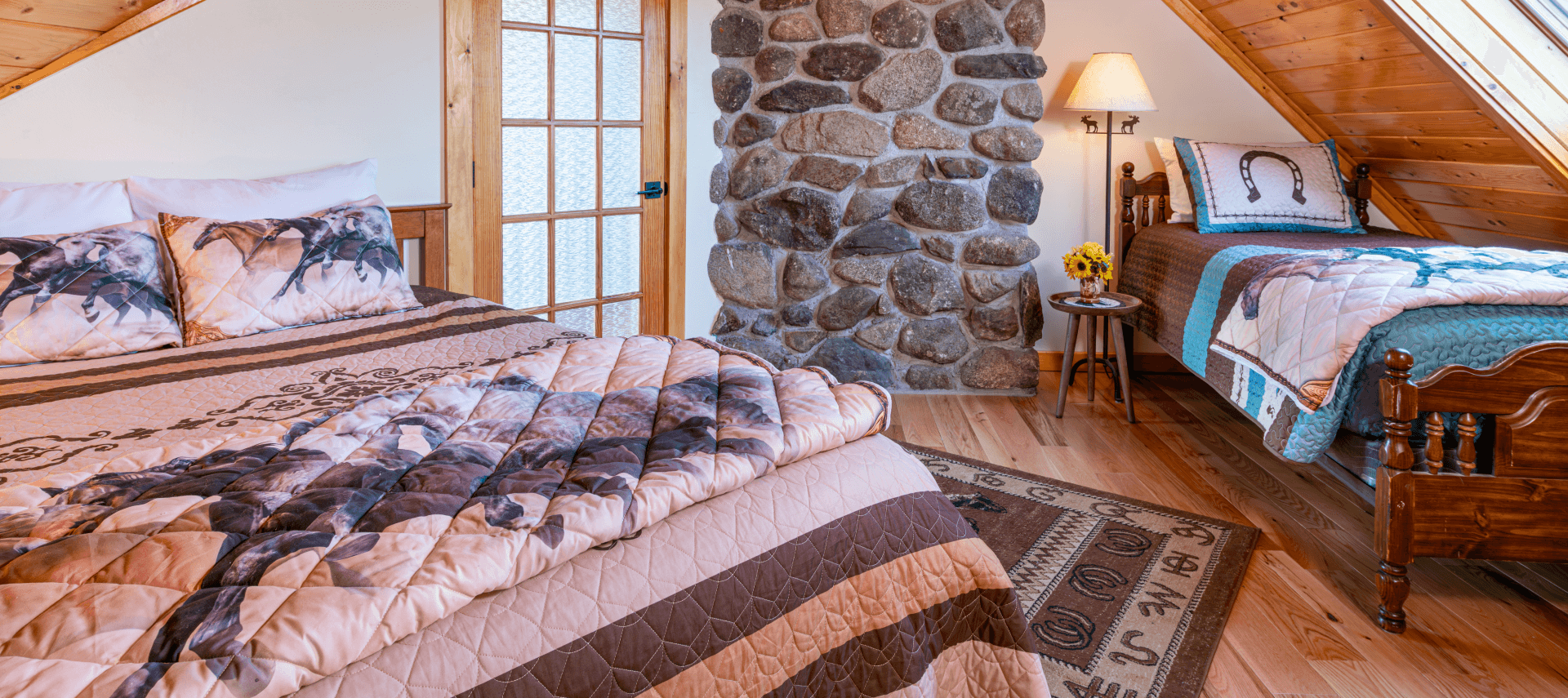 Queen and twin bed in front of a fieldstone chimney with horse throw blankets