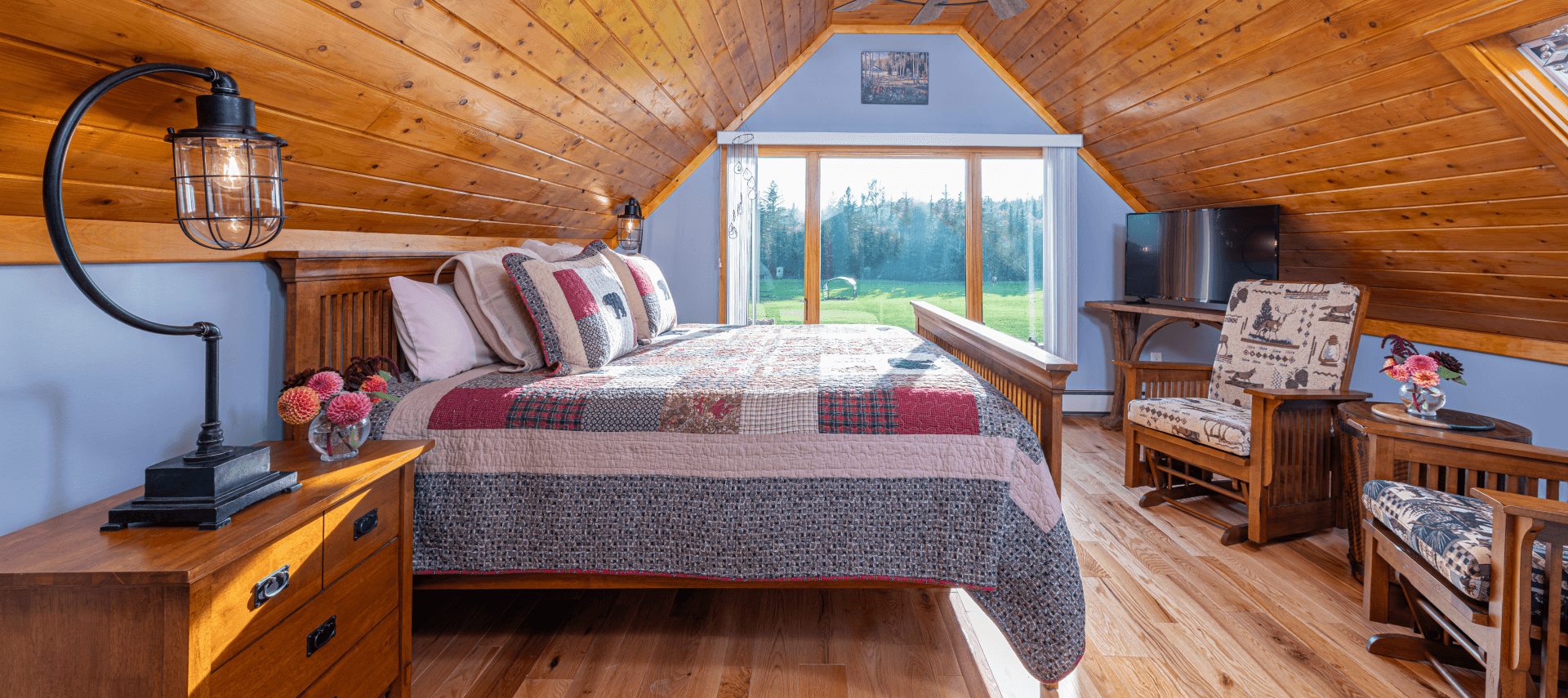 King bed with patchwork quilt in front of large window overlooking a pasture