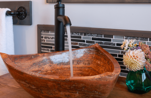 Triangular reddish brown vessel sink with water flowing from faucet.
