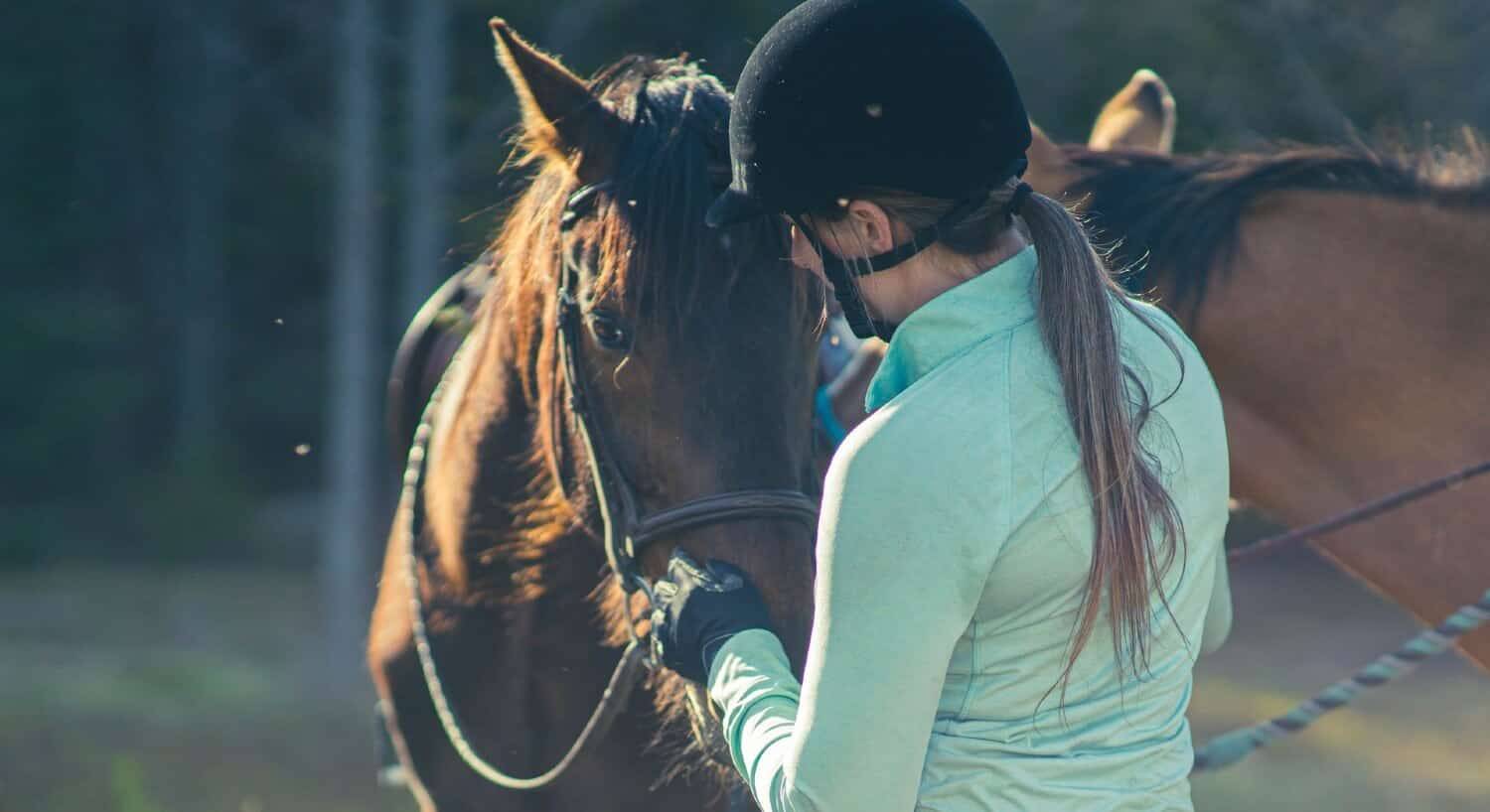 A woman in a green shirt and black helmet petting the face of a brown horse