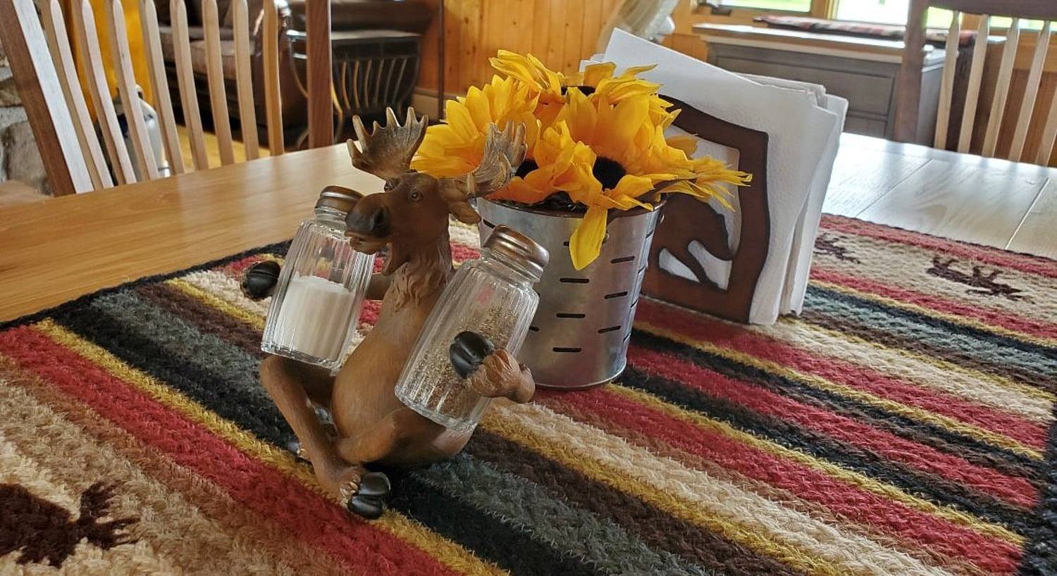 Kitchen table with a moose ornament holding salt and pepper shakers and tin vase with sunflowers